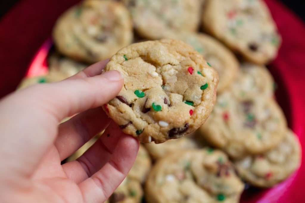 A hand holding a Christmas cake batter cookie with red and green circle sprinkles.