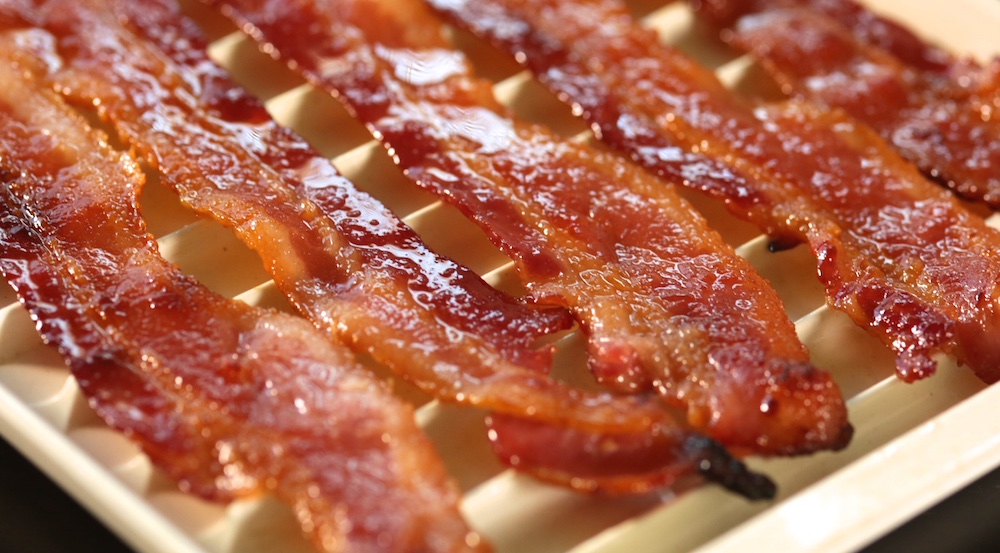 Five pieces of candied bacon sit next to each other on a drying rack.