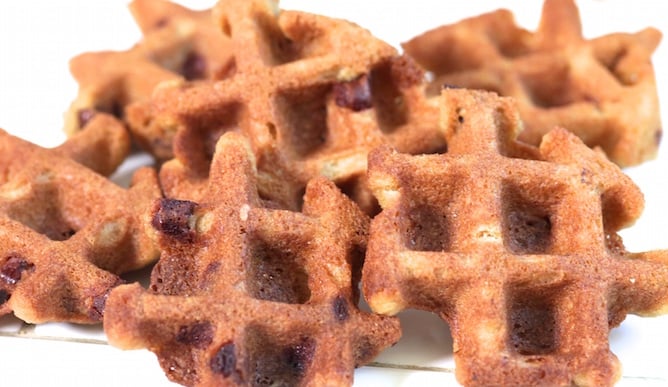 A pile of chocolate chip cookies that have been cooked in the waffle maker sit on a white background