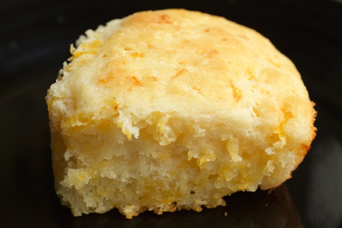 A thick cheesy buttermilk biscuit on a black background