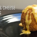 A fried Mac and cheese ball covered in cheese sauce on a black plate