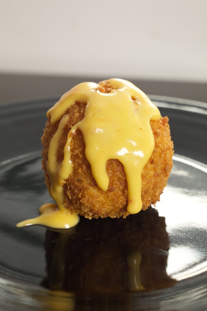 A fried Mac & cheese ball covered in cheese sauce