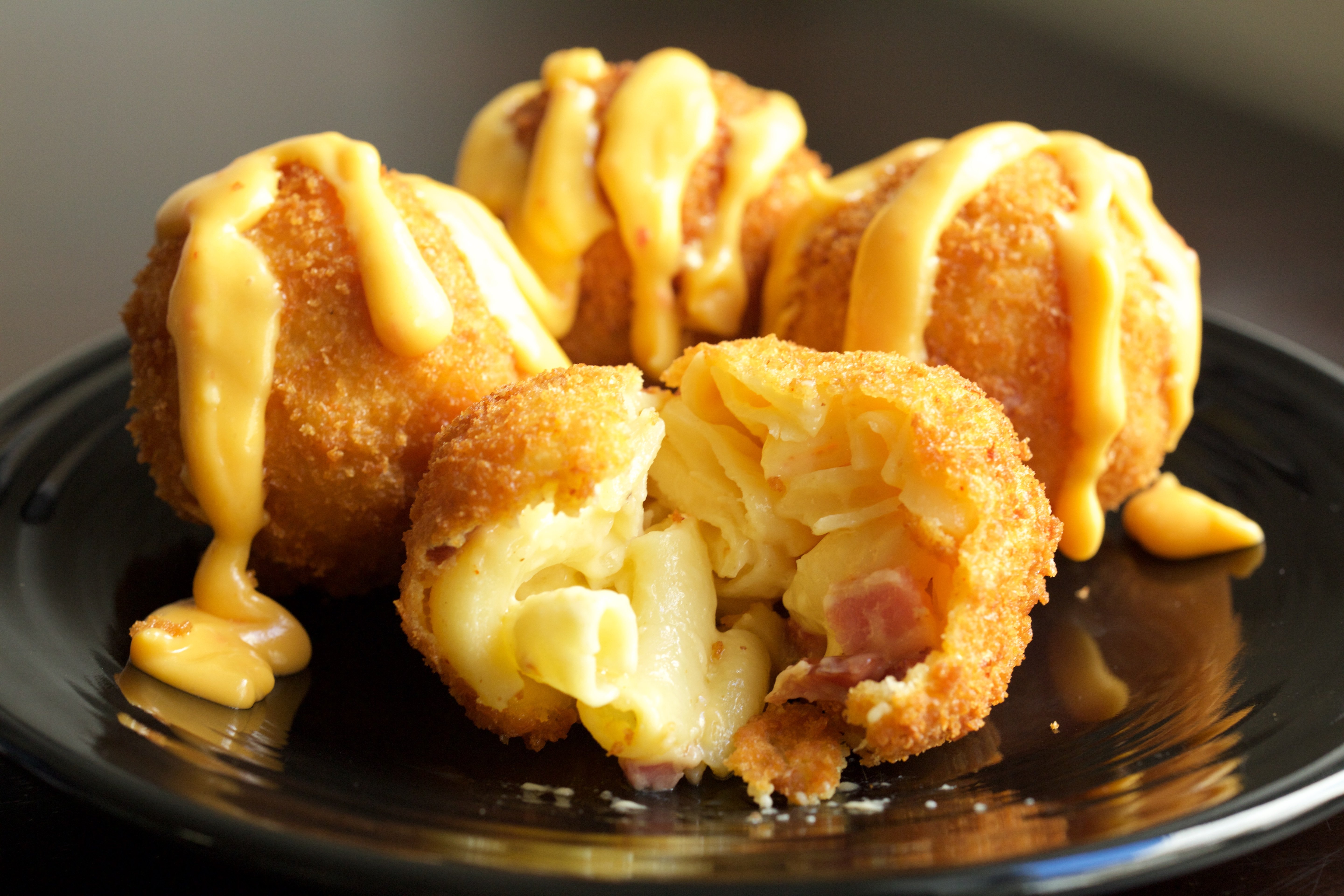 Four fried macaroni and cheese balls on a black plate