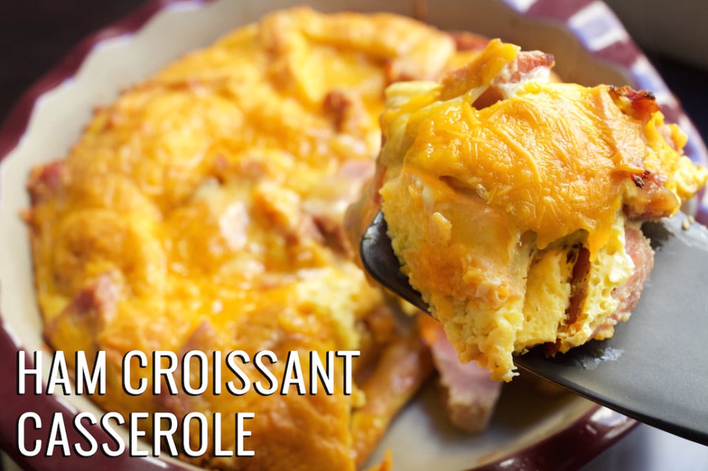 A spatula holds up a piece of ham and croissant breakfast casserole with the casserole dish in the background