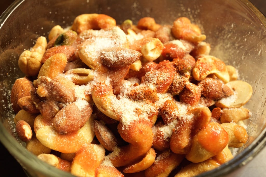 Mixed nuts in a glass bowl covered in spices, salt, and hot sauce - the ingredients for buffalo spiced nuts.