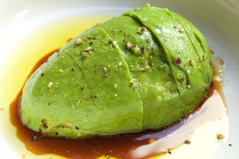 A sliced marinated avocado sits in a white bowl with soy sauce and olive oil