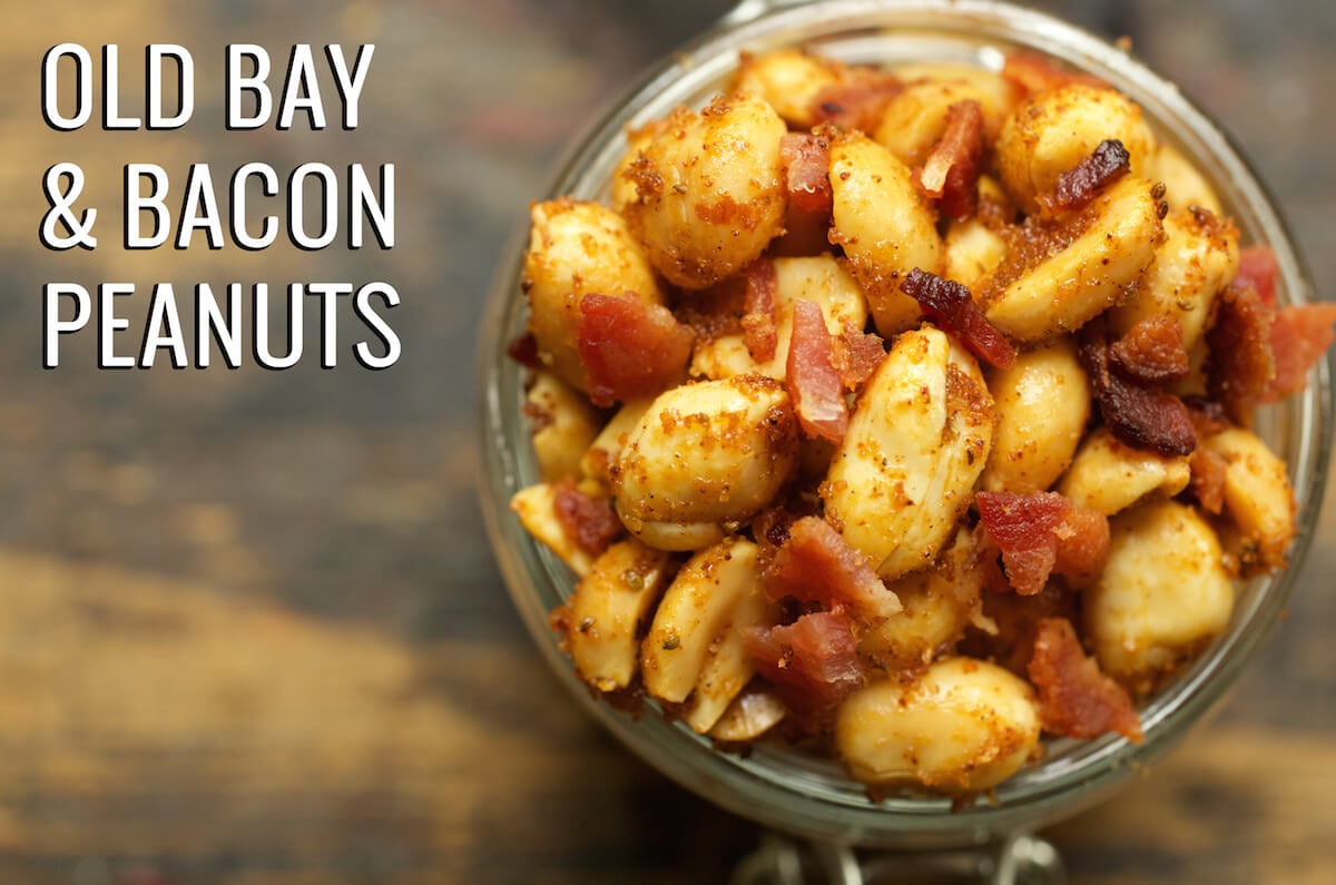 Overhead look at a glass jar filled to the top with Old Bay & bacon peanuts. Text in the upper left corner reads "Old Bay & Bacon Peanuts".