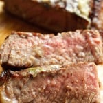 Two sliced pieces of steak cooked medium rare in front of the rest of the steak on a cutting board