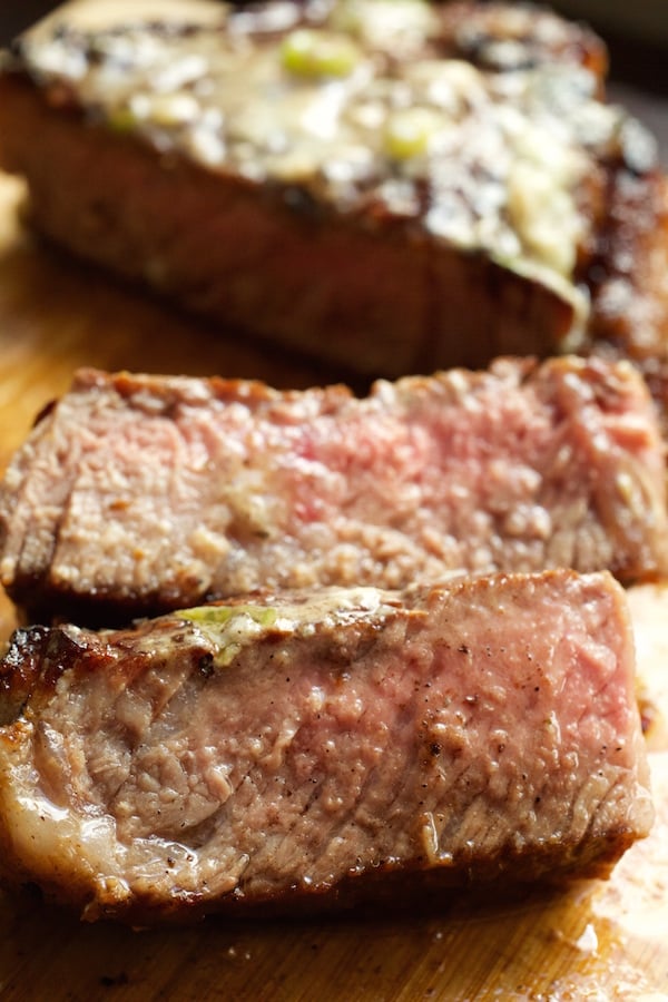 Two sliced pieces of steak cooked medium rare in front of the rest of the steak on a cutting board