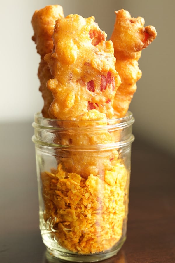 A mason jar with crushed Doritos on the bottom. Fried bacon sits on top.