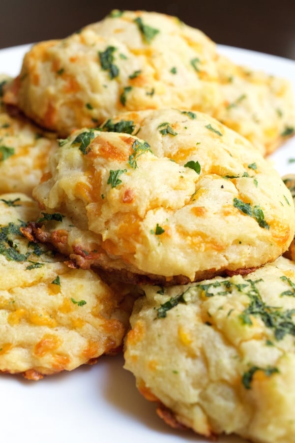 Homemade cheddar bay biscuits stacked on a white plate.