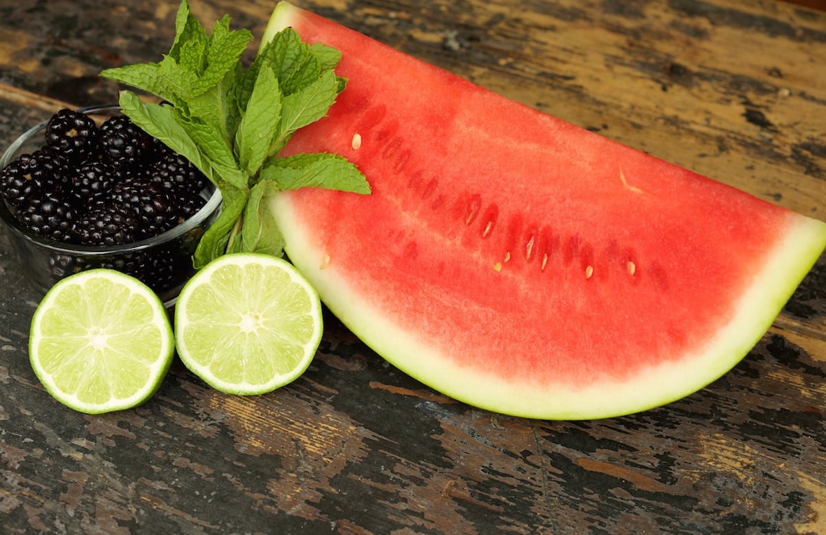 Sliced watermelon, slice lemon, a bowl of blackberries, and a bunch of fresh mint.