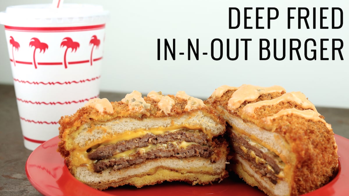 A deep-fried In-N-Out cheese burger sits on a red plate in front of the classic palm tree In-N-Out soda cup.