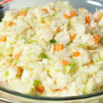 A large glass bowl is filled with a homemade version of KFC's coleslaw. It has chopped green cabbage and chopped carrots.