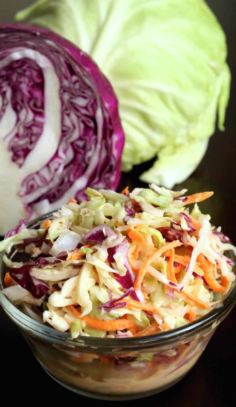 A small glass bowl of copycat KFC coleslaw sits in front of a cabbage head sliced in half.