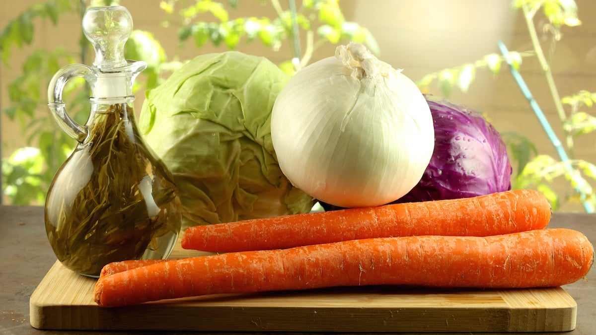 KFC Coleslaw Ingredients on a cutting board. Carrots, tarragon vinegar, onion, purple cabbage and green cabbage.