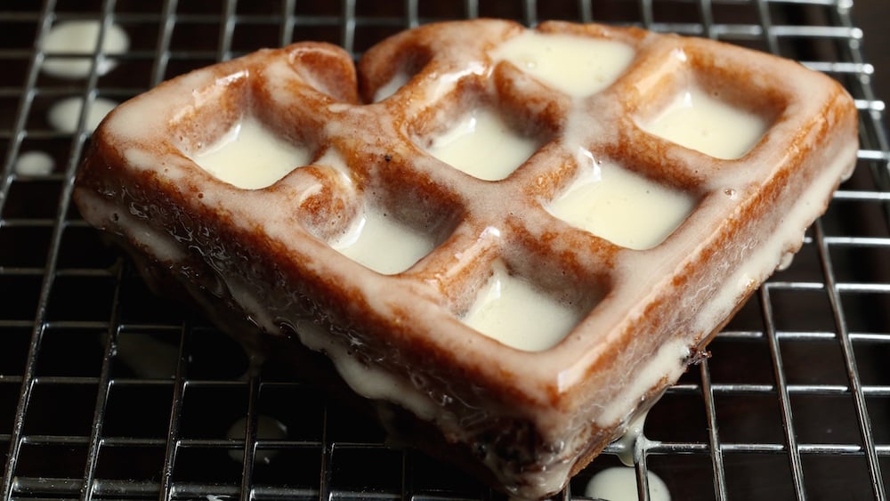 An Apple Fritter Waffle Donut on a cooling rack after being glazed.