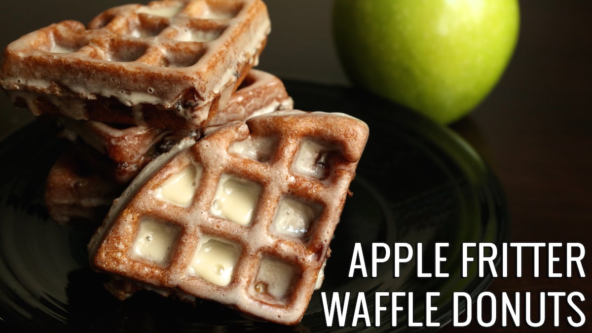 Apple Fritter Waffle Donuts on a black plate with a green apple in the background.