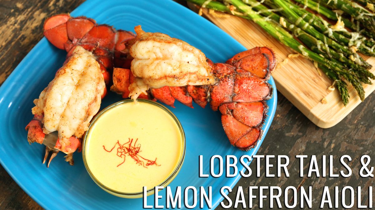 Two cooked lobster tails sit on a plate next to a small bowl of lemon saffron aioli. Text reads "Lobster Tails with Lemon Saffron Aioli"