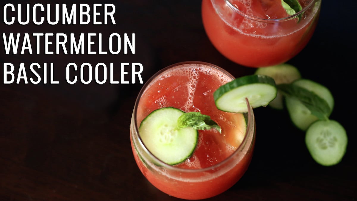 A pink-red drink in a stemless wine glass garnished with sliced cucumber and basil. Text reads "Cucumber Watermelon Basil Cooler"