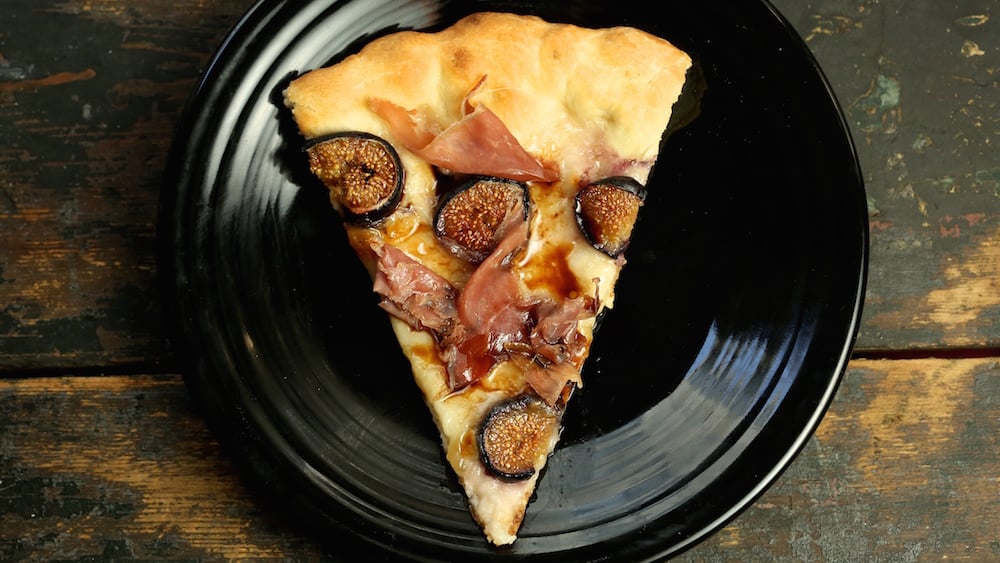 A plate with a slice of pizza topped with figs prosciutto and balsamic drizzle.