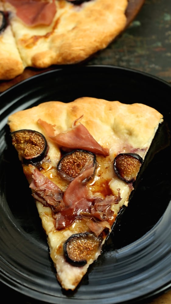 A single slice of fig and prosciutto pizza on a black plate. 