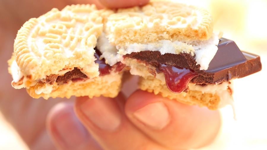 A close up of a golden oreo s'more that's been bitten into, showing the raspberry filling drip out of the chocolate.