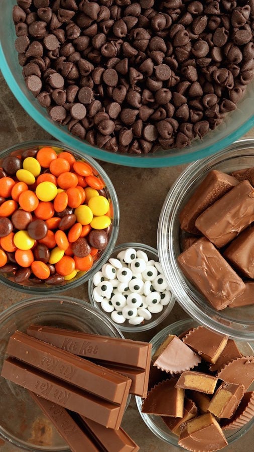 Overhead view of Halloween candy bark ingredients - mini chocolate chips, Reese's pieces, edible candy eyes, kit kats, chopped Reese's cups and mini candy bars.