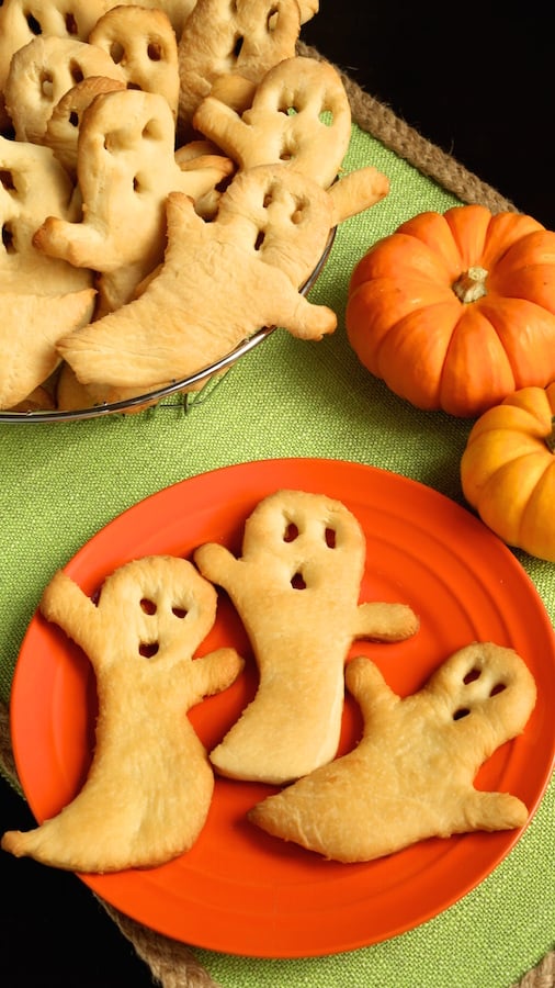 Three Halloween Ghost Crisps laid out on an orange plate with a bowl full of them in the background.