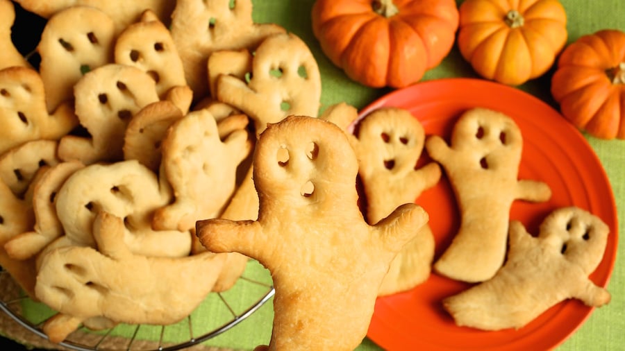 A hand holds up a single ghost shaped crisp. In the background there is a basket full of them.