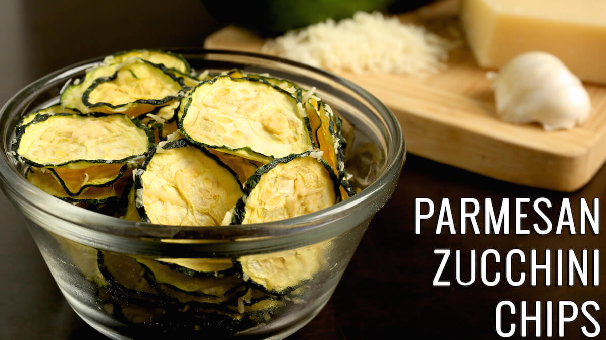 A small glass bowl is full of dehydrated zucchini slices. Text reads "Parmesan Zucchini Chips"