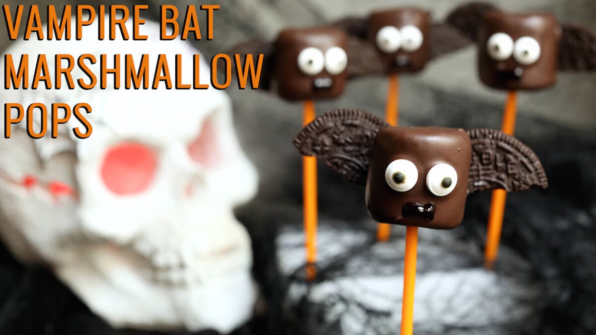 Large marshmallows that have been dipped in chocolate, then had half an oreo added to each side and candy eyes attached to look like a bat. Text reads "Vampire Bat Marshmallow Pops"