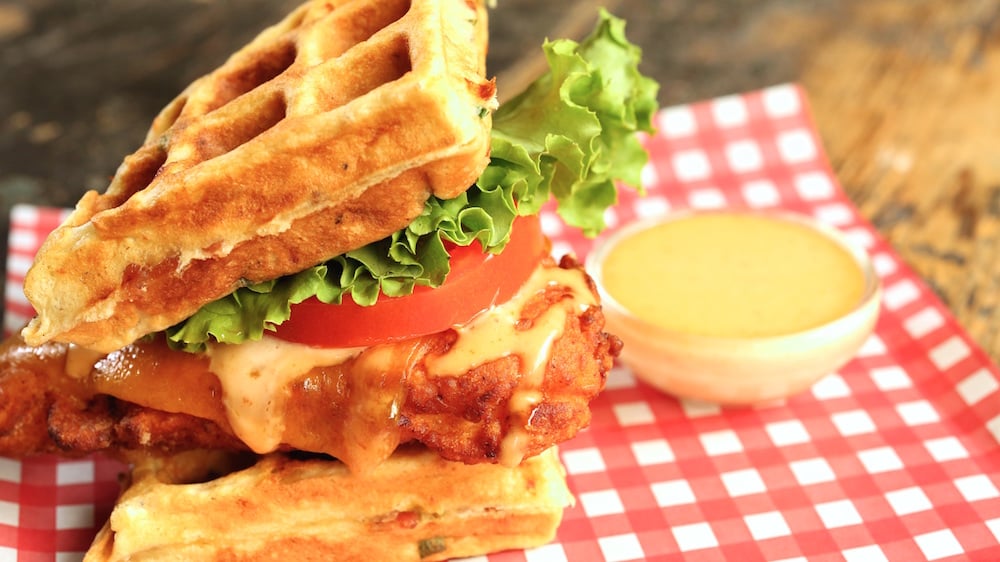 A fried chicken sandwich between two waffles with lettuce, tomato, and sriracha aioli. 