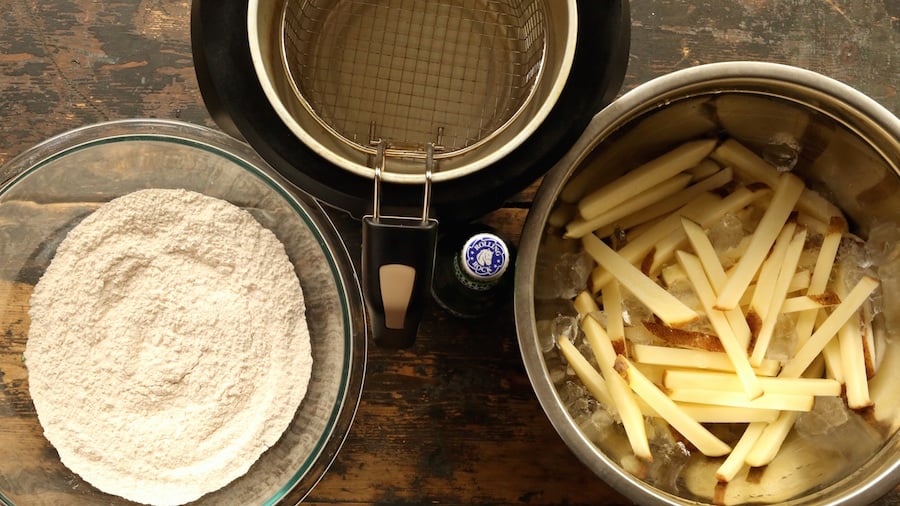 Over head view of bottle of beer, deep fryer, sliced potatoes, and batter.