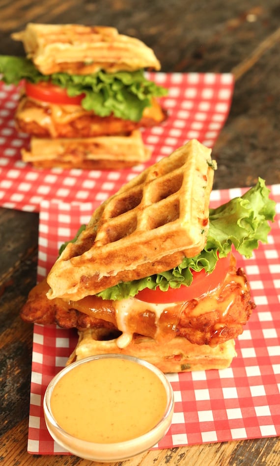 Two Fried Chicken and Bacon Cheddar Waffle Sandwiches next to a bowl of maple sriracha aioli.