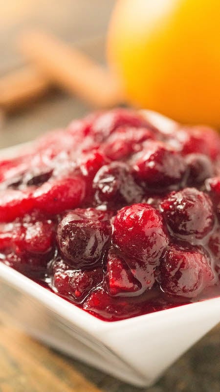 Homemade Holiday Cranberry Compote Sauce in a white serving dish. Orange and cinnamon sticks out of focus in the background.