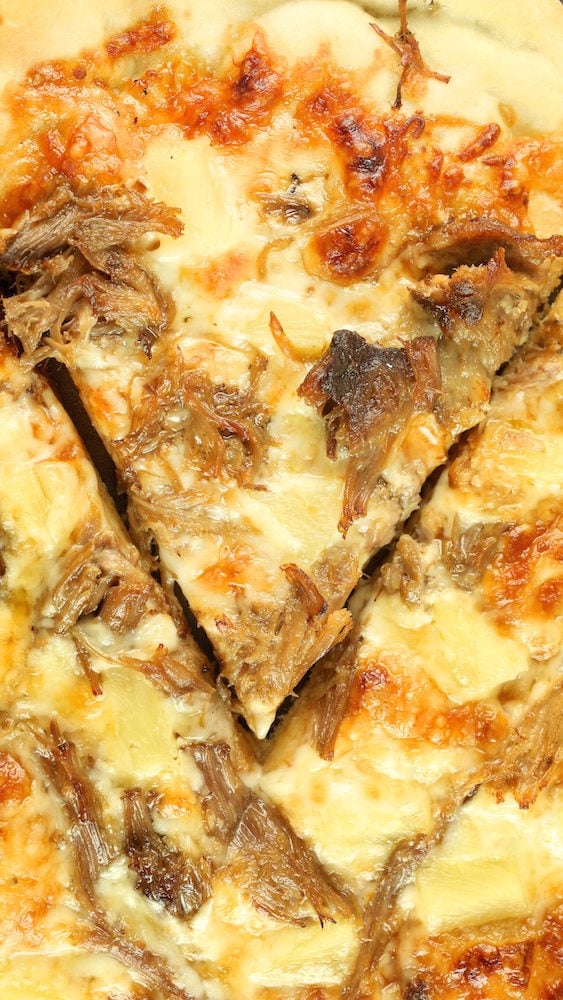 A slice of Kalua pork pizza with pineapple has been cut