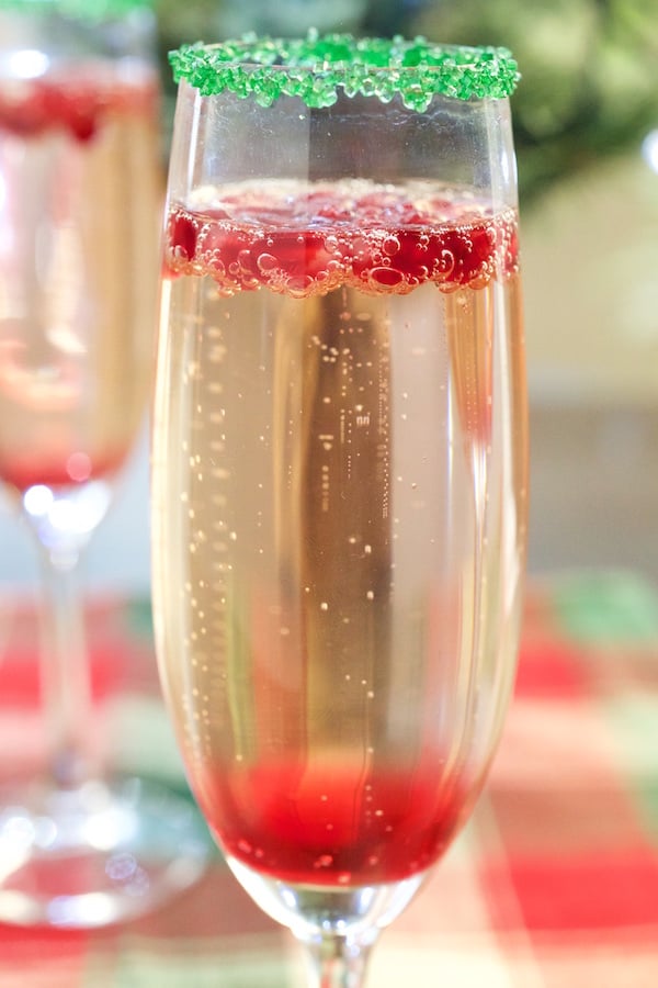 Christmas Champagne Cocktail with layers of pomegranate simple syrup, champagne, and fresh pomegranate. Green sugar rim.