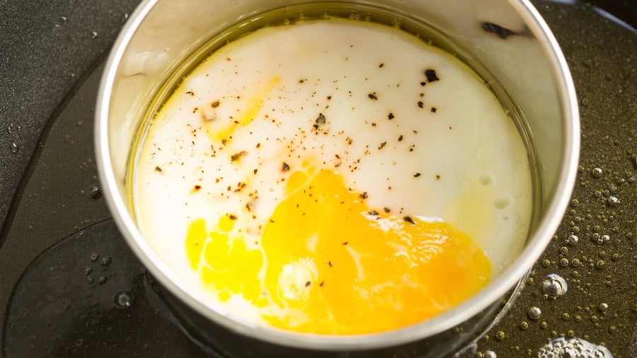 An egg cooking inside a metal ring on a skillet to form a "bun"