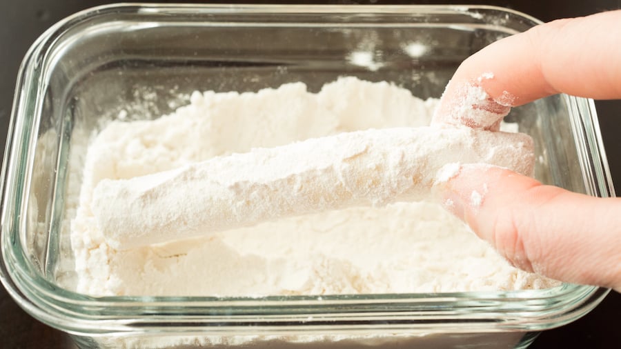 A cheese stick being rolled in flour