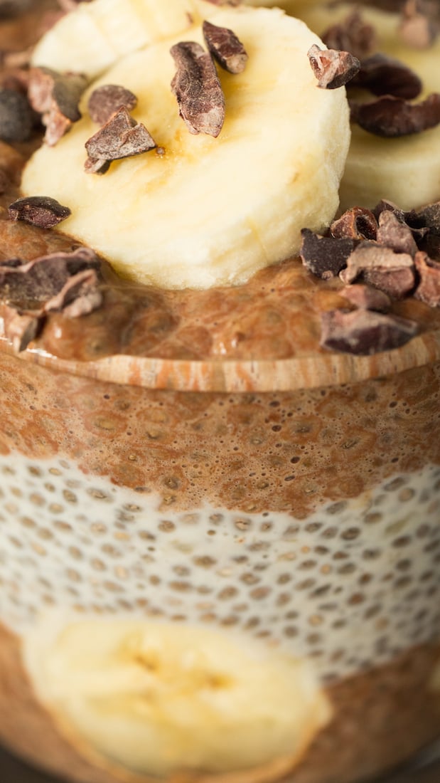 Extreme close up of a Cacao Banana Chia Seed Pudding featuring the alternating layers of chocolate chia pudding and vanilla chia pudding. Sliced banana and cacao nibs are on top.