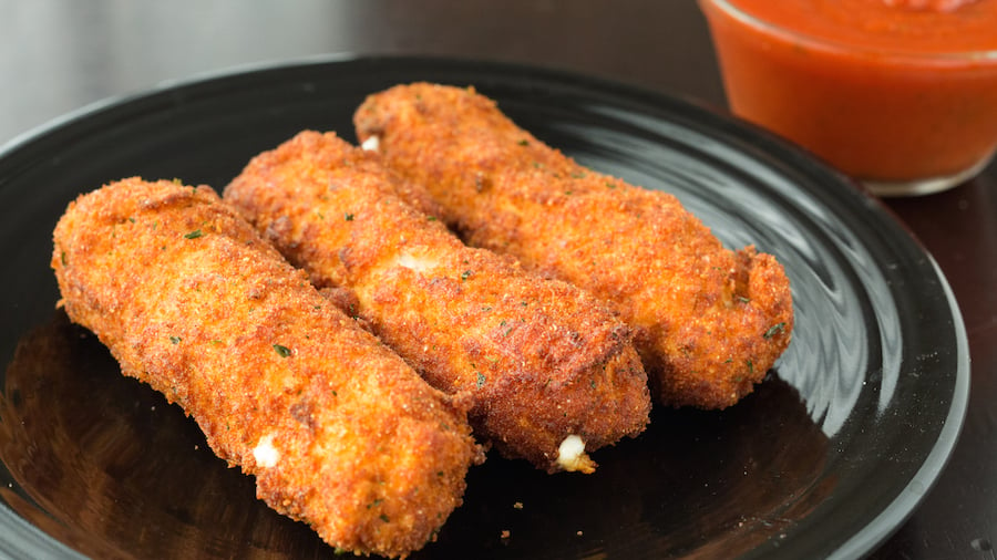 Three deep fried mozzarella chicken cheese sticks on a black plate next to marinara dipping sauce.