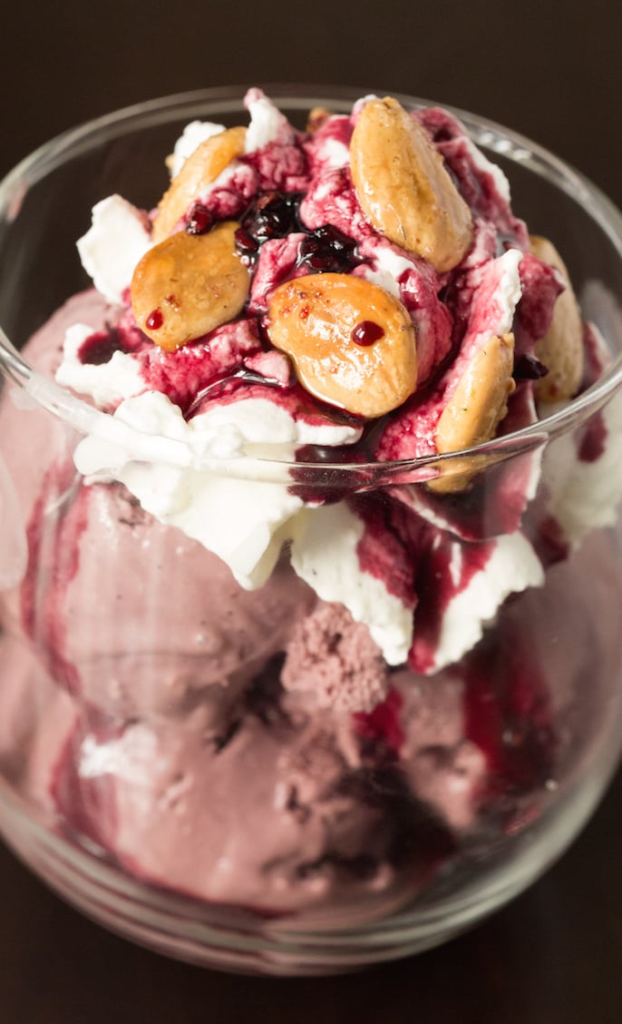 Red Wine Ice Cream Sundae with Vanilla Bean Whipped Cream, Spiced Red Wine Syrup, and Lavender Almonds in a wine glass on a black background