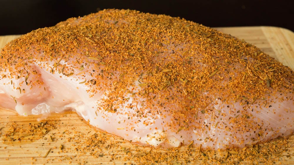 Raw chicken breast on a cutting board covered in blackening seasoning.