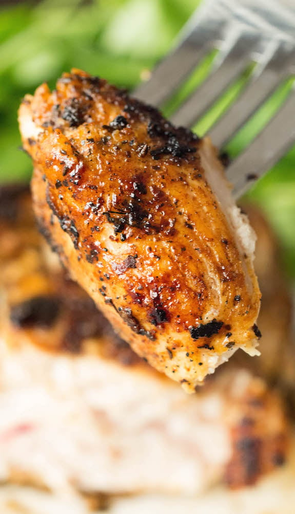 A cut piece of cooked blackened chicken being held up by a fork. The rest of the chicken breast sits out of focus in the background.