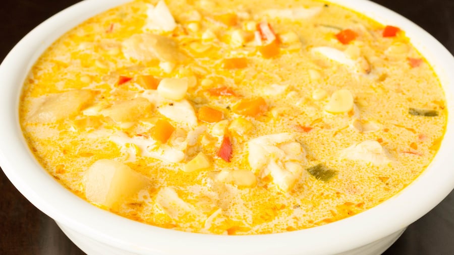 A bowl of corn and crab chowder in a white bowl before being topped with potato chips.