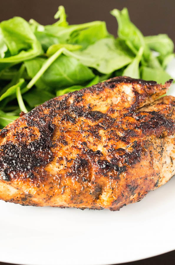 A close up of a blackened chicken breast with a side of spinach on a white plate.