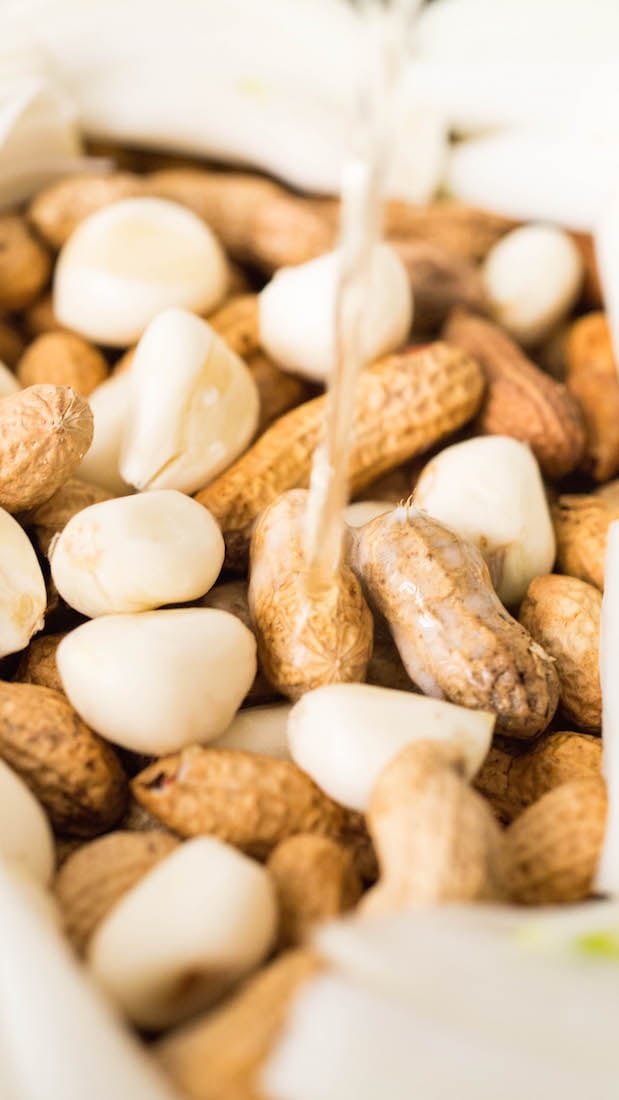 A close up of beer being poured on top of the peanuts and garlic cloves.