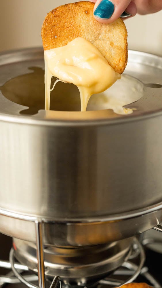 A homemade potato chip after being dipped into the beer cheese fondue. The cheese is dripping off the chip back into the pot.