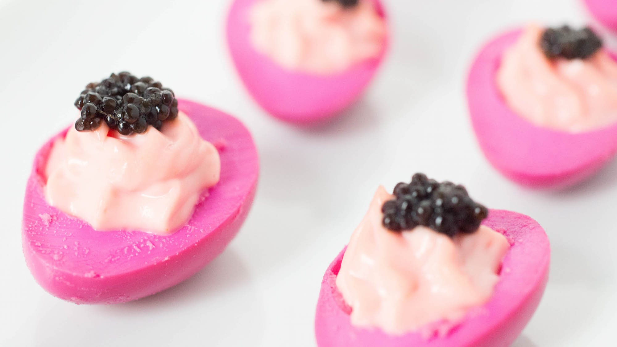 A close up showing four pink deviled quail eggs with dollops of caviar on top.
